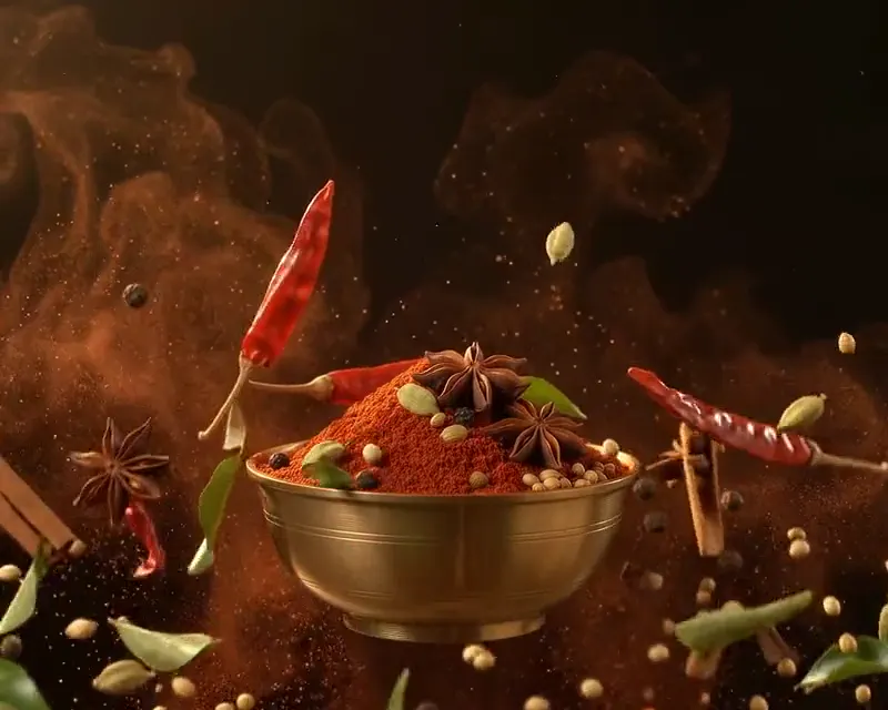 Whole spices and red masala dust bursting out of a brass bowl of homemade masala